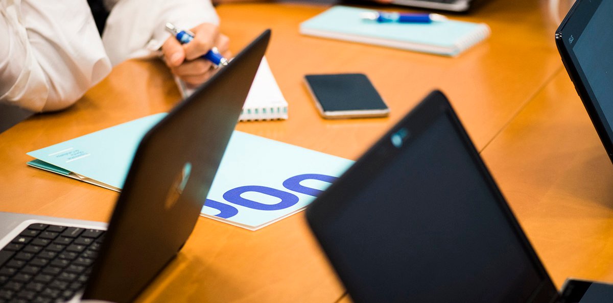 Diverses persones reunides al voltant d'una taula a sobre de la qual hi ha portàtils i una carpeta amb el logo de la UOC