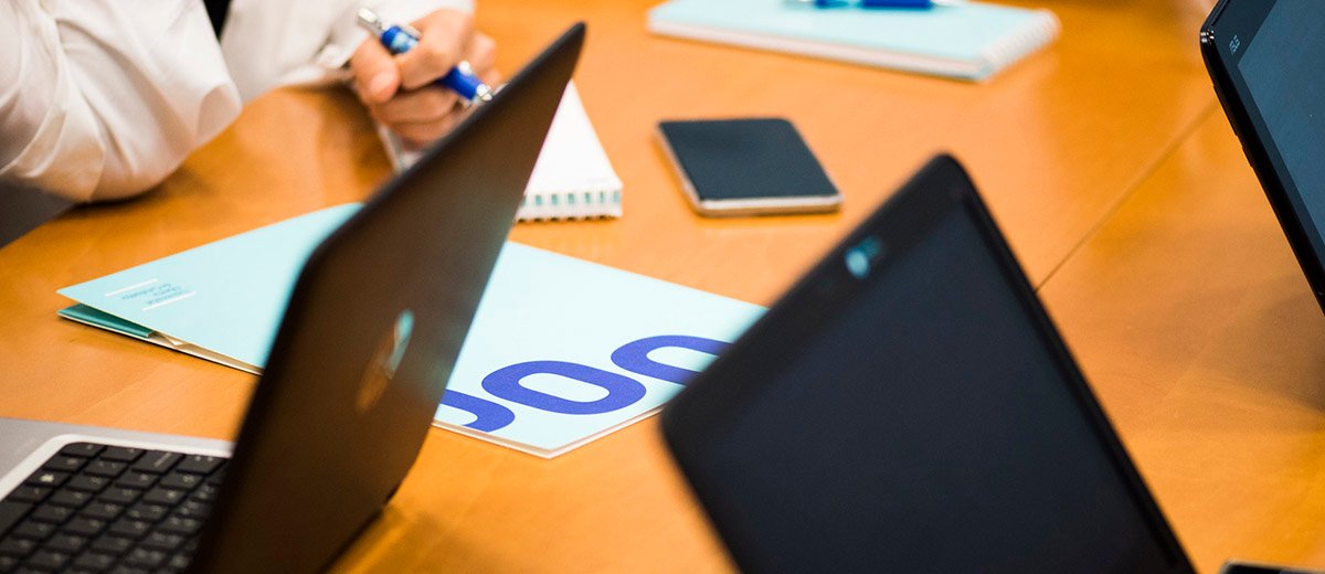 Diverses persones reunides al voltant d'una taula a sobre de la qual hi ha portàtils i una carpeta amb el logo de la UOC