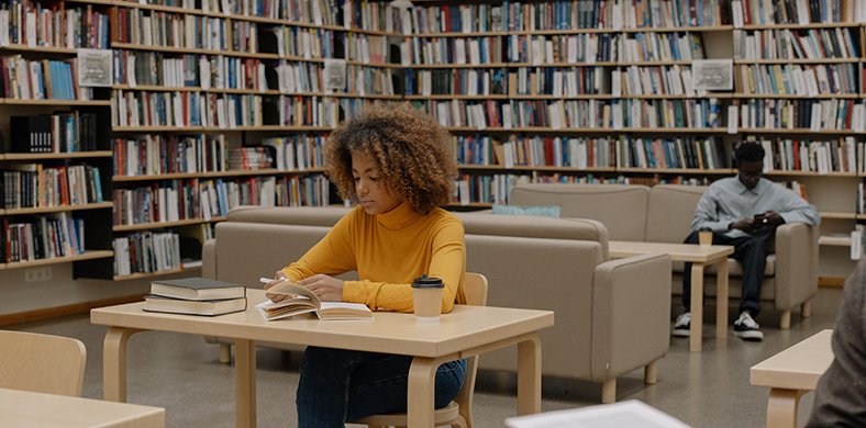 Dos personas leyendo y estudiando dentro de una biblioteca