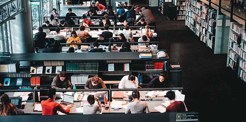 Una sección de una biblioteca con mesas llenas de gente trabajando y estudiando