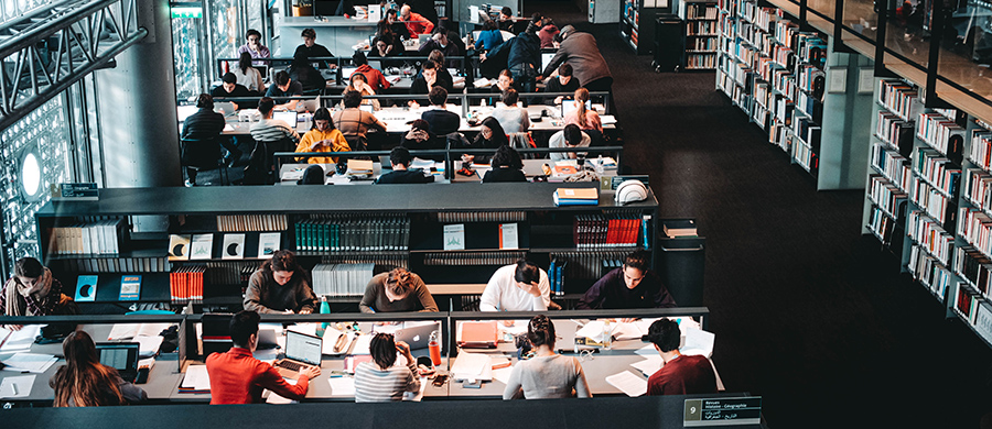 Una sección de una biblioteca con mesas llenas de gente trabajando y estudiando