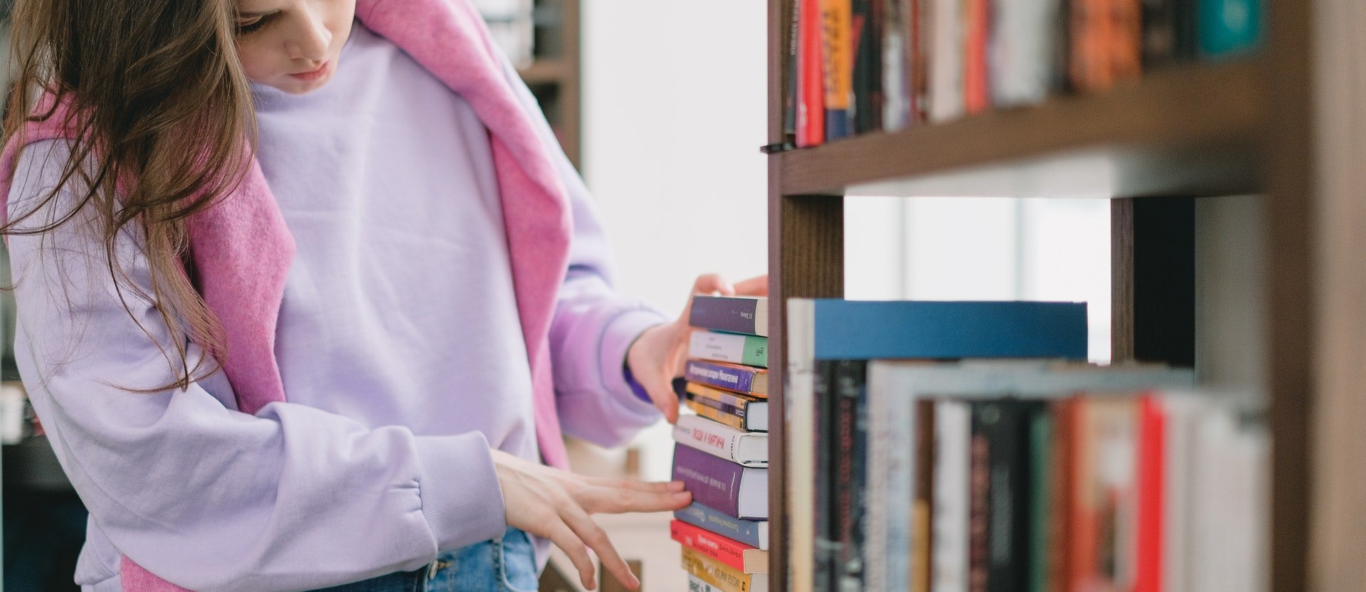 Noia col·locant llibres a una biblioteca