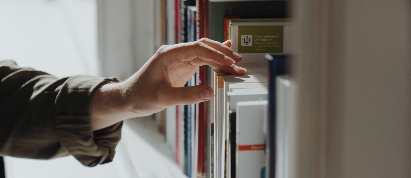 Una mano retirando un libro de una estantería