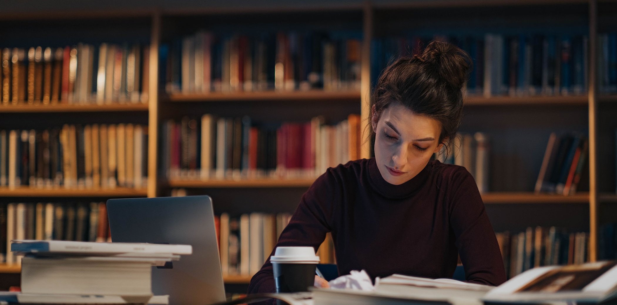 Una dona escrivint a una taula plena de papers i llibres