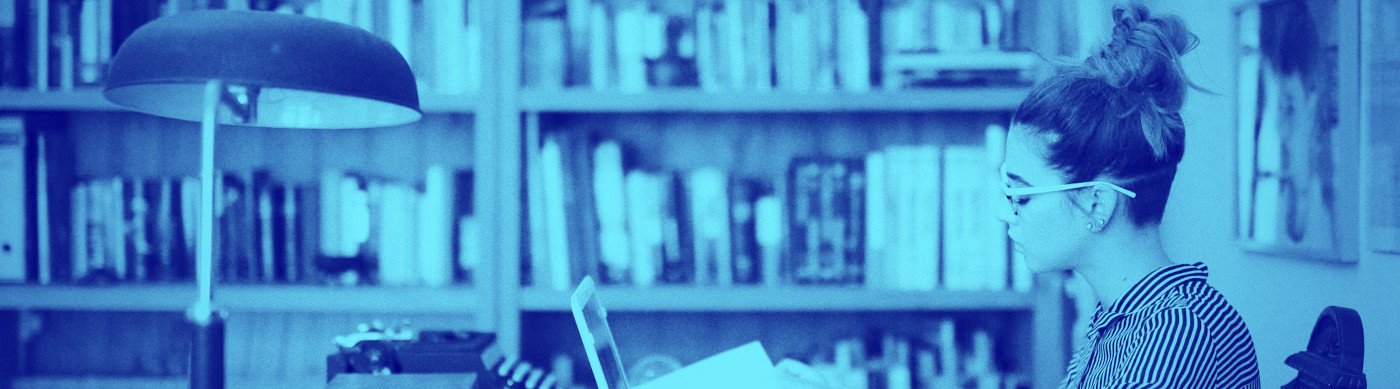 Una mujer con un portátil y un grupo de papeles en la mesa de una biblioteca